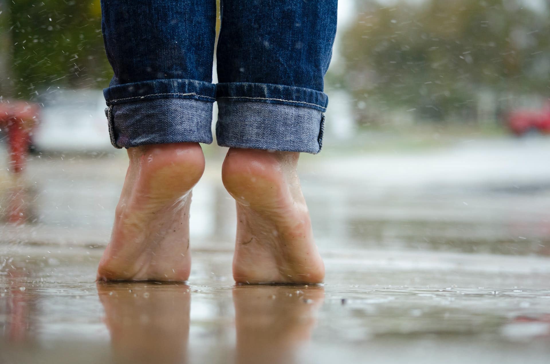 Nackte Füße die im Regen auf Zehenspitzen auf Asphalt stehen