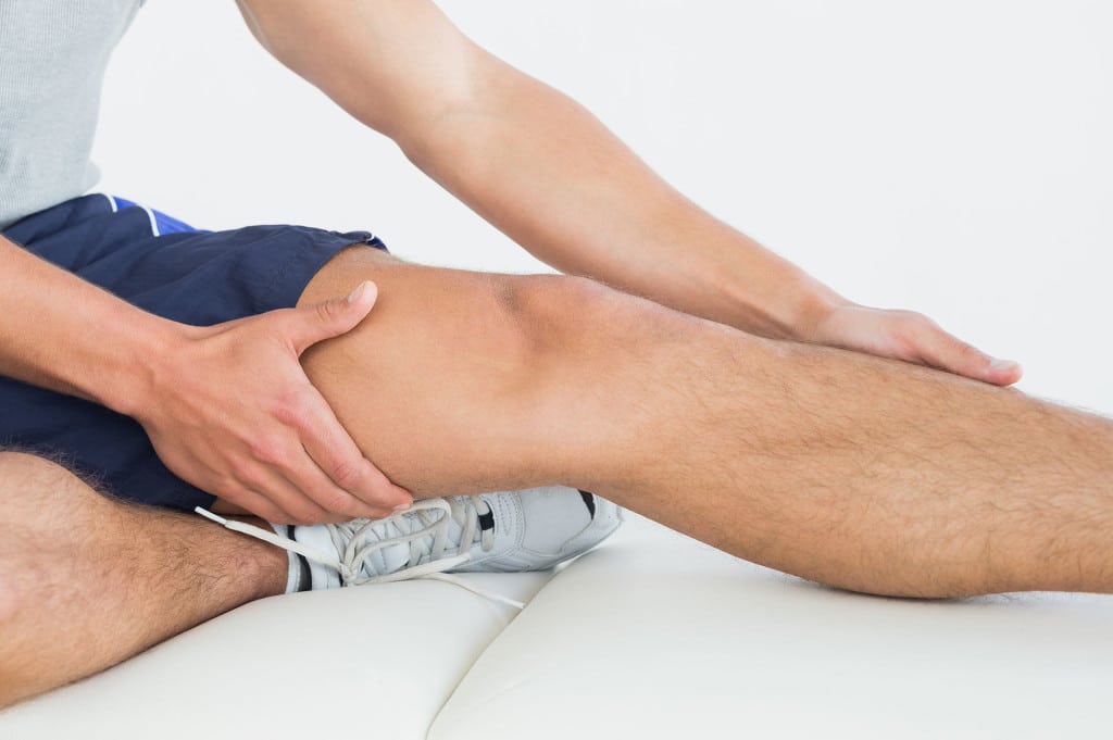 Ein Sportler sitzt und greift sein schmerzendes Bein