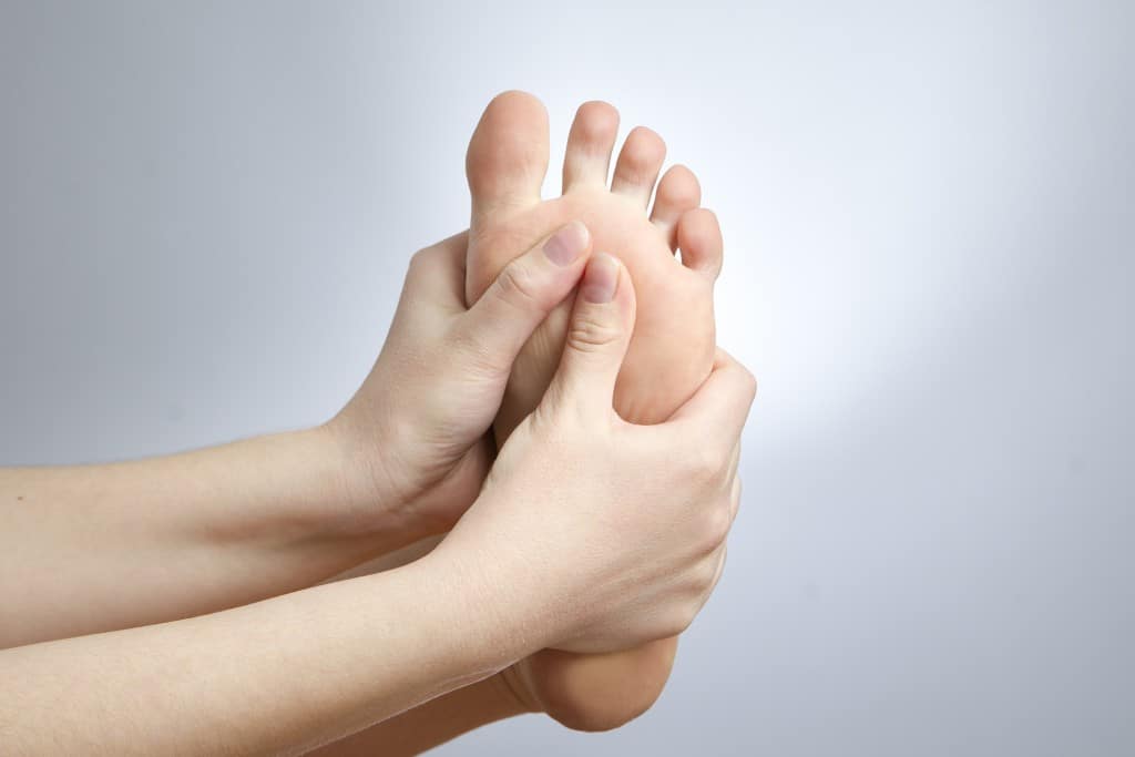 Eine weibliche Person greift mit beiden Händen ihren Fuß