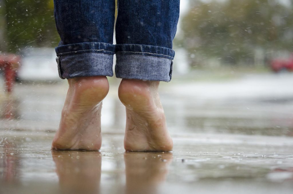 Nackte Füße die im Regen auf Zehenspitzen auf Asphalt stehen