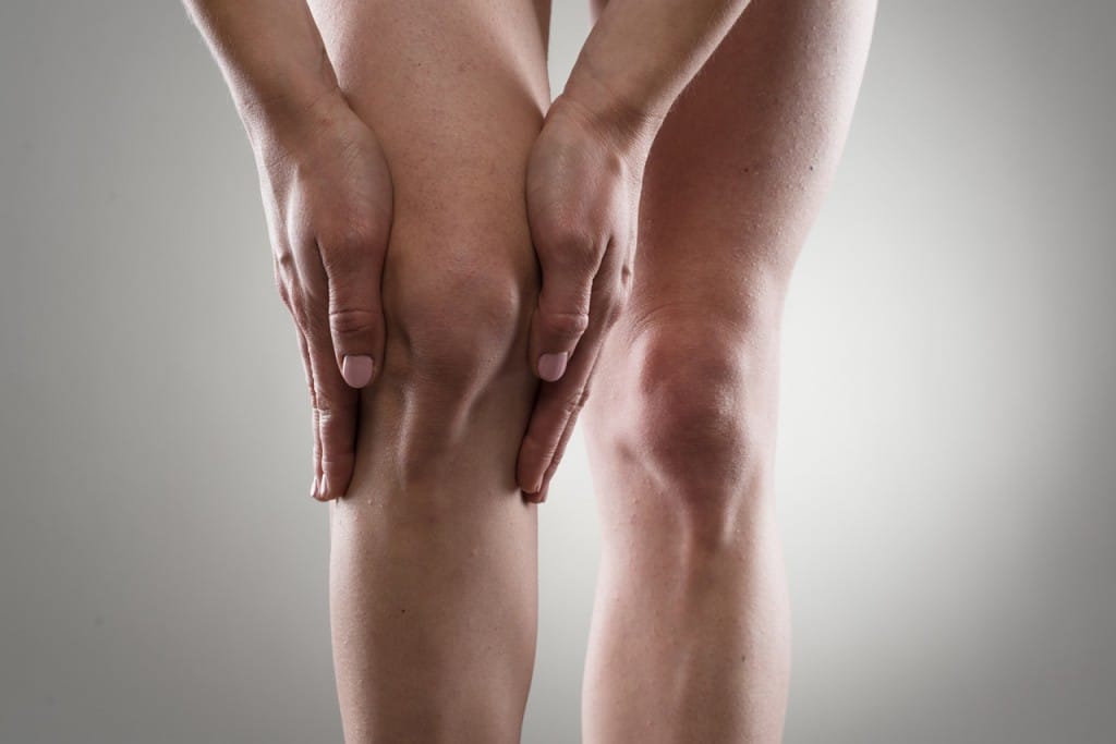 Eine weibliche Person greift sich mit beiden Händen an Ihr Knie