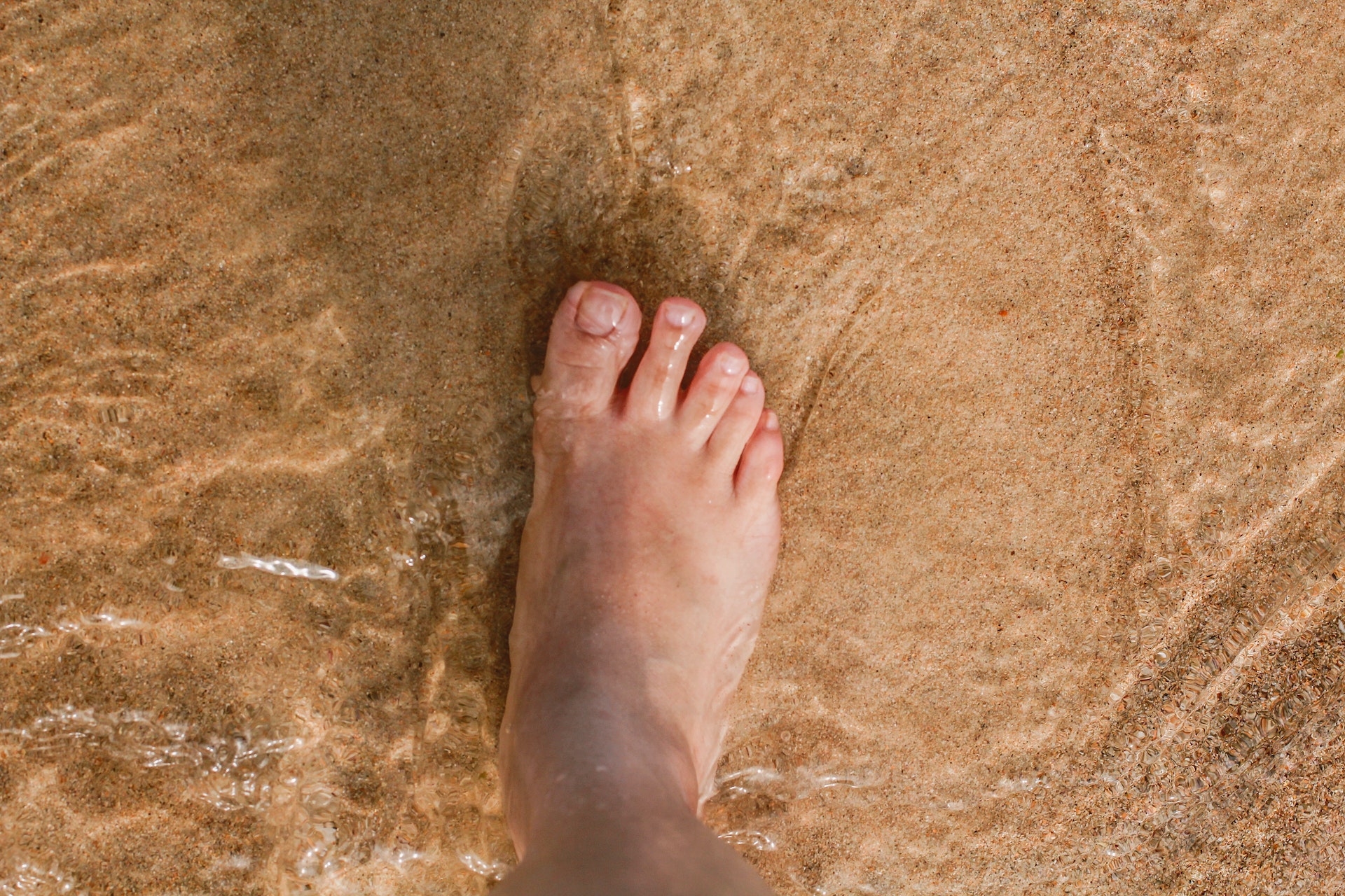 Ein Fuß in sehr niedrigem klarem Wasser an einem Sandstrand